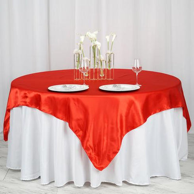 Red satin tablecloth draped over a round table with elegant dinnerware.
