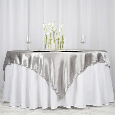 Elegant silver tablecloth draped over a round table with glass vases and wine glasses.