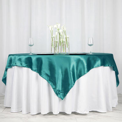Teal satin tablecloth draped over a white table, elegant dining setup.