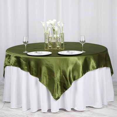 Green satin tablecloth draped over a round table with plates and glasses.