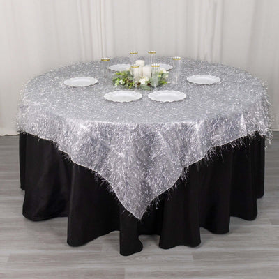 Round silver tablecloth with fringed edges on a black table, set with plates and candles.