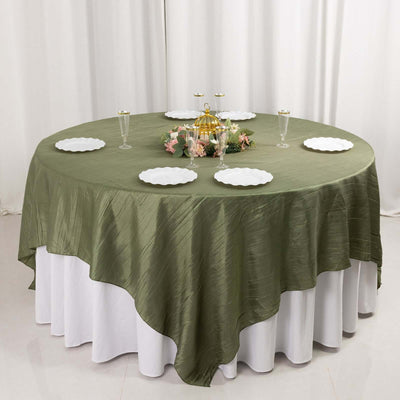 Round olive green tablecloth draped elegantly over a white table with plates and decor.