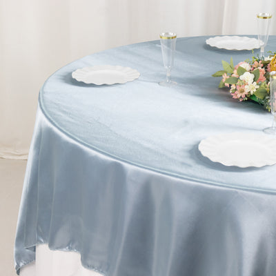 Round table with blue satin tablecloth, white plates, and floral centerpiece.