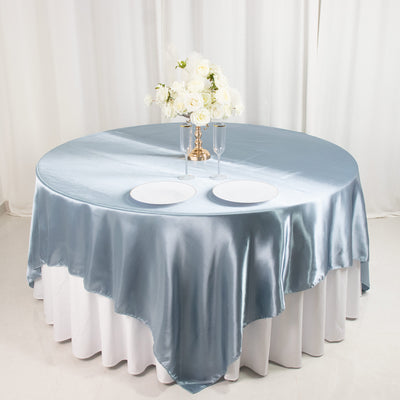 Blue satin round tablecloth with white underlay and elegant floral centerpiece.