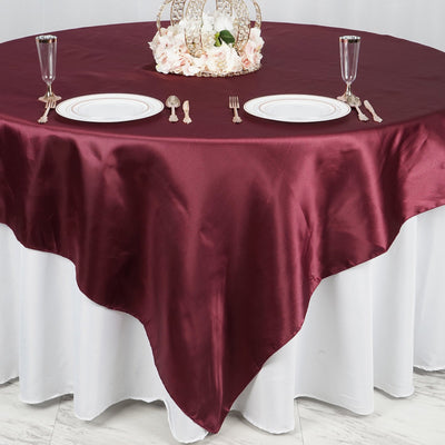 Burgundy satin tablecloth on a white table with elegant dinnerware set.