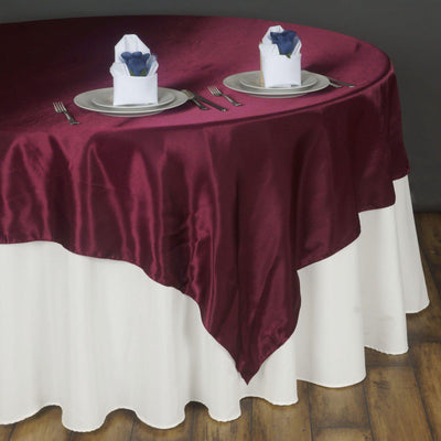 Burgundy tablecloth draped over a white table with napkin holders.