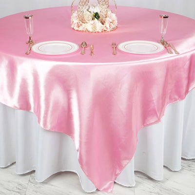 Pink satin tablecloth draped over a round table with elegant table settings.