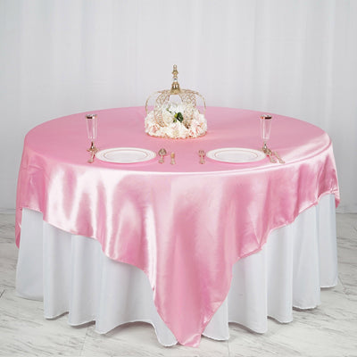 Pink satin tablecloth draped over a round table set for a formal dining occasion.