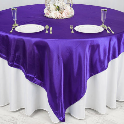 Purple satin tablecloth draped elegantly over a round table setting with dinnerware.