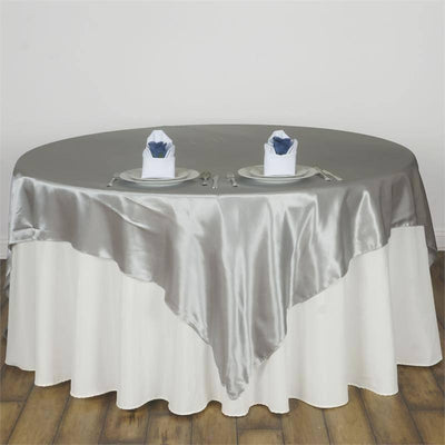 Elegant round table with a silver satin tablecloth and napkins on plates.