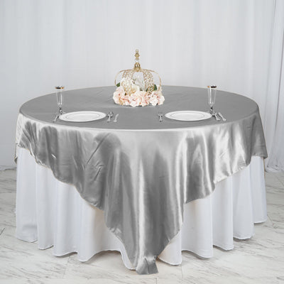 Elegant round table set with a silver satin tablecloth and floral centerpiece.
