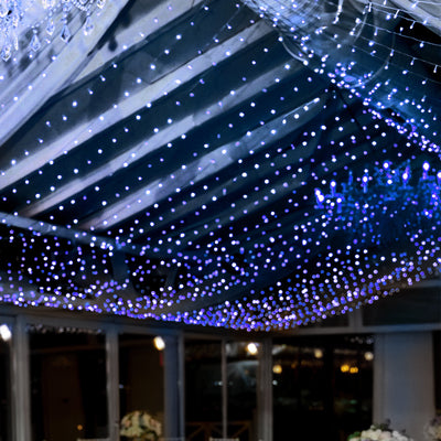 Twinkling blue and white fairy lights draped across a wedding venue ceiling.