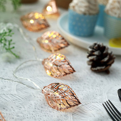 Copper leaf string lights on a white table with cupcakes and pinecones.