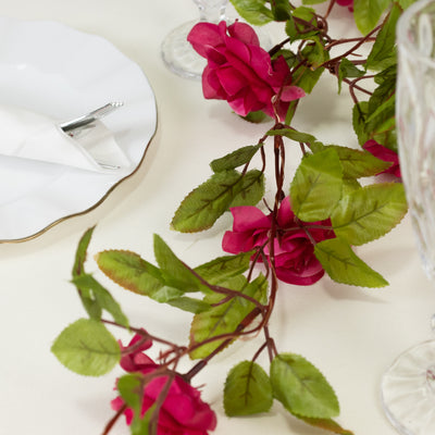 Artificial pink rose garland with green leaves on a table setting.