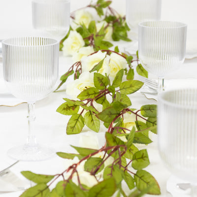 Table setting with clear ribbed glasses and floral greenery centerpiece.