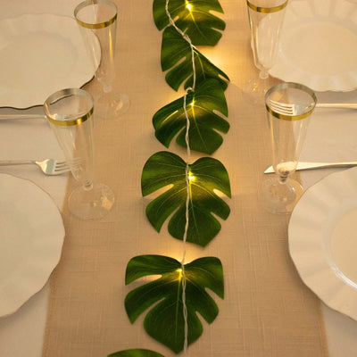 Table setting with tropical leaf runner and lights on a dining table.