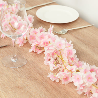 Pink artificial flower garland on a dining table with glassware and plates.