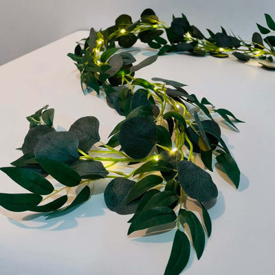 Artificial greenery garland with LED lights on a plain background.