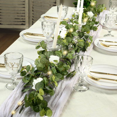 Elegant table centerpiece with greenery and white flowers for dining setup.