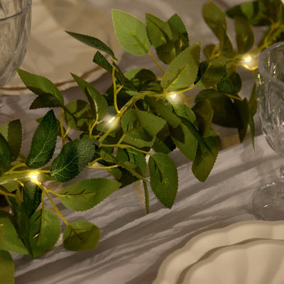 Green leaf garland with fairy lights on a table setting.