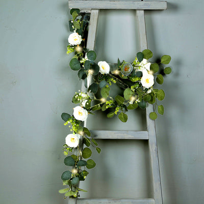 Floral arrangement with white roses and greenery on a rustic ladder.