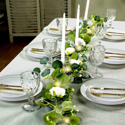 Elegant dining table setting with candles, greenery, and glassware.