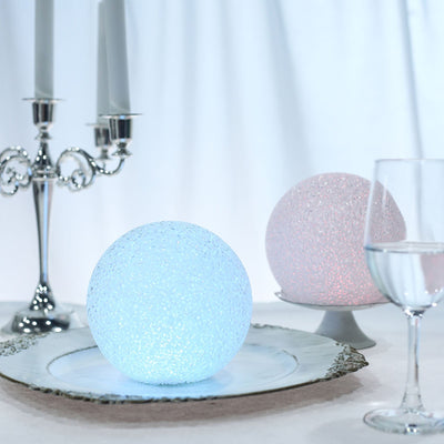 Glowing decorative spheres in blue and pink on a silver platter with candle holders.