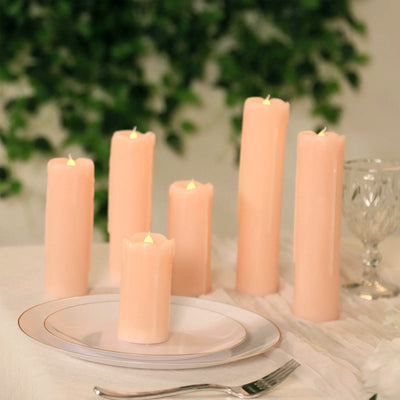 Set of soft pink LED candles on a table with greenery backdrop.
