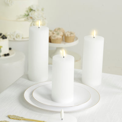 White ribbed candles on a table with a white plate and dessert in the background.