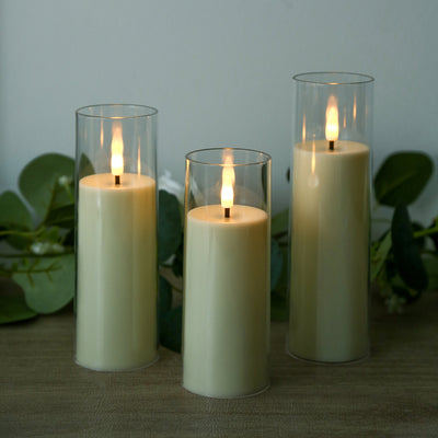 Three lit pillar candles in glass holders with green leaves background