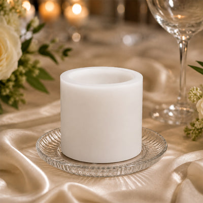 White pillar candle on glass plate with elegant wedding table setting