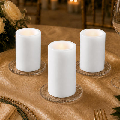 Three white LED pillar candles on glass holders at a gold table setting
