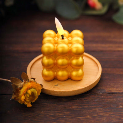 Golden bubble candle on a wooden plate with a dried flower.