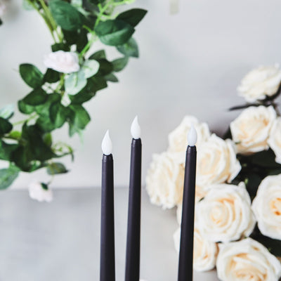 Black taper candles with white tips beside cream roses and greenery.