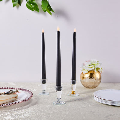 Three black taper candles in glass holders on an elegant table setting.