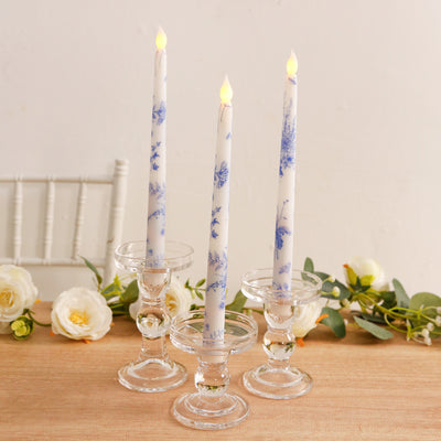 Blue floral taper candles in elegant glass holders on a wooden table.
