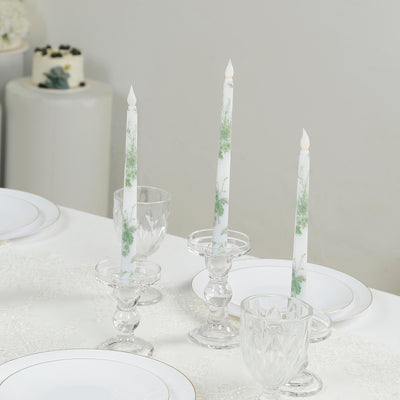 Elegant floral-patterned candles in crystal holders on a dining table.