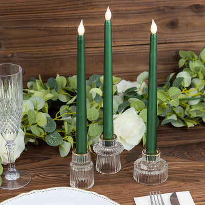 Green tapered candles in crystal holders on a rustic wooden table with greenery.