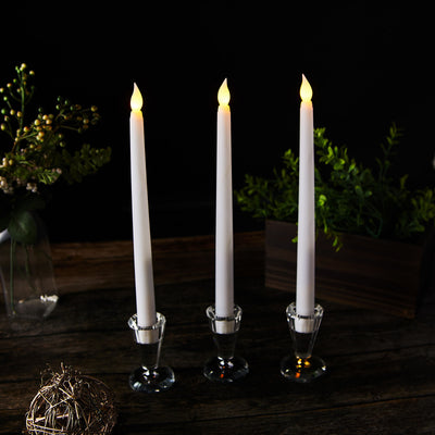 Three elegant white taper candles in glass holders, glowing softly against a dark background.