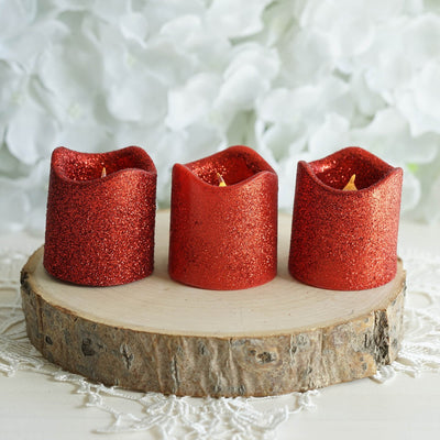 Three red glitter candles on a wooden slice with a floral background.
