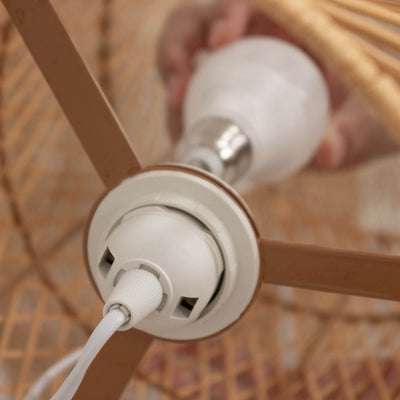Light fixture socket with a hand adjusting the bulb in a woven lamp shade.