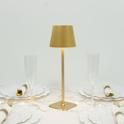 Gold table lamp with pleated shade on a dining table setting.