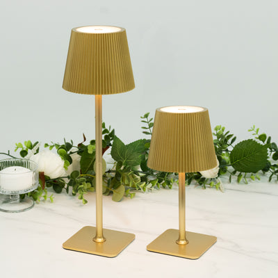 Gold pleated lamps in two sizes with greenery backdrop.