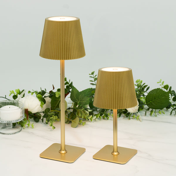 Gold pleated lamps in two sizes with greenery backdrop.