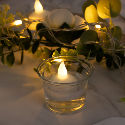 LED tea light candle in a glass holder with decorative greenery.