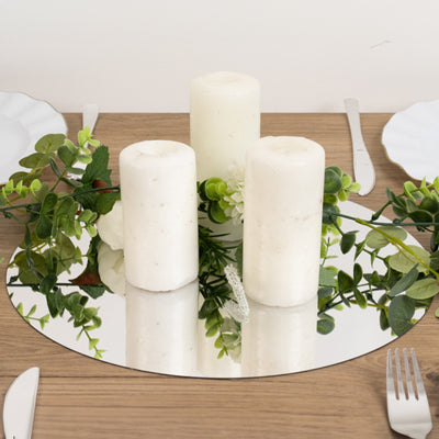 White pillar candles with greenery on a mirrored table setting.