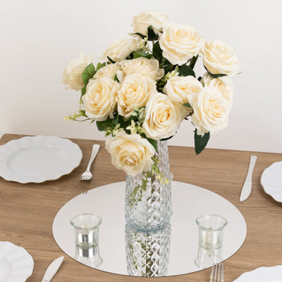 Cream roses in a crystal vase on a mirrored table setting.
