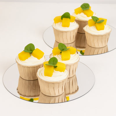 Mango cupcakes with cream and mint leaves on mirrored plates.