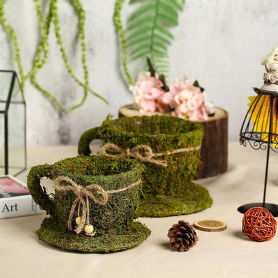 Moss-covered decorative cups with twine accents on a tabletop.