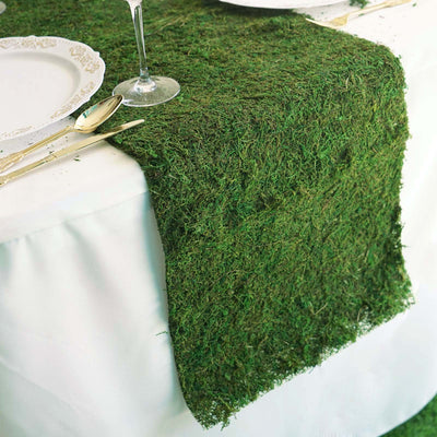 Green moss table runner on a white table setting with plates and cutlery.